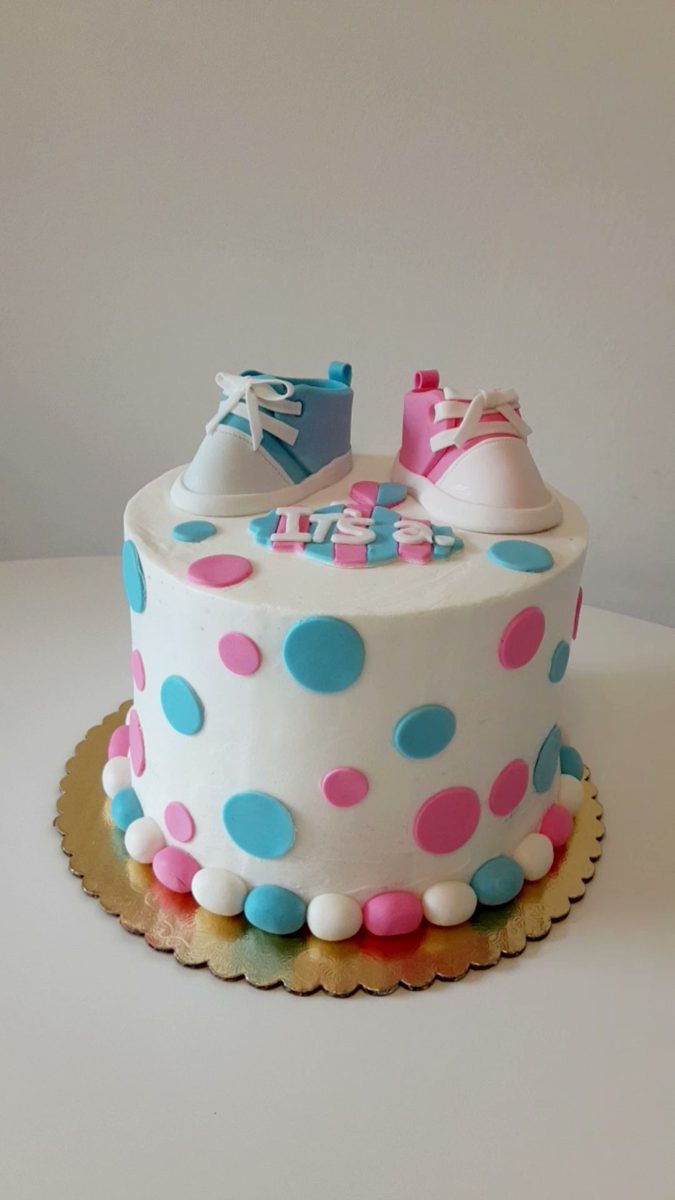 White cake with pink and blue polka dots topped with baby shoe decorations