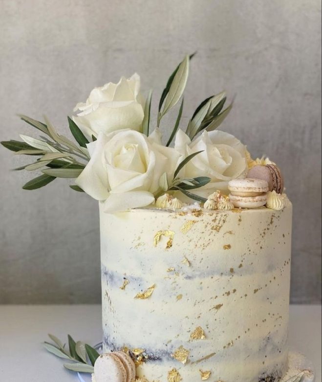 White custom cake decorated with white roses, gold leaf, and macarons