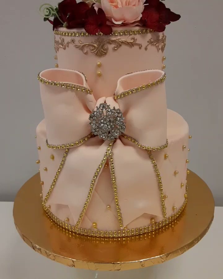 Two-tier pink cake with a large fondant bow and gold detail